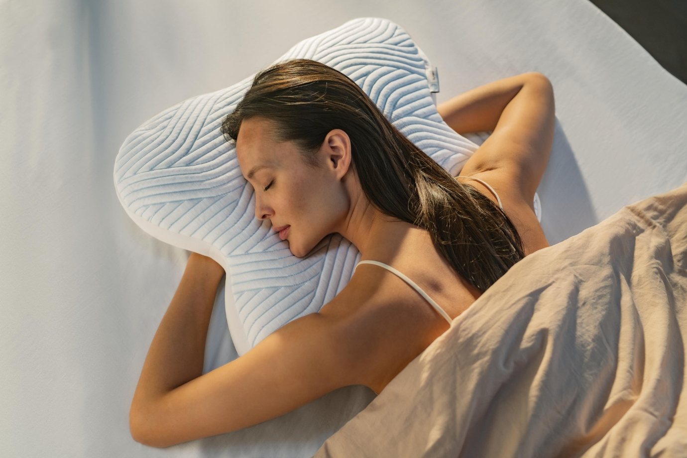 Beautiful brunette woman sleeping on a strangely shaped ombracio tempur pillow with smart cooling technology.
